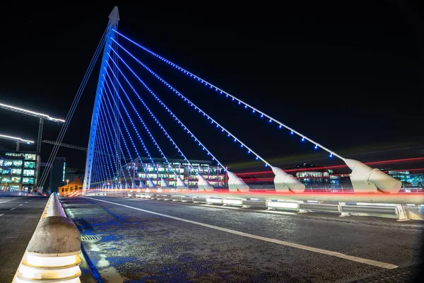 Road across an illuminated suspension bridge and light trails left by passing vehicles at night. Dublin, Ireland.