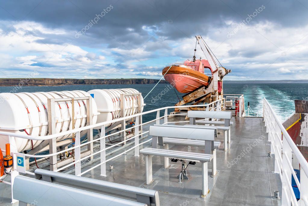 Empty upper deck of a ferry boat in navigation with a lifeboat and other safety equipment on a stormy spring day. Orkney Islands, Scotland, UK.