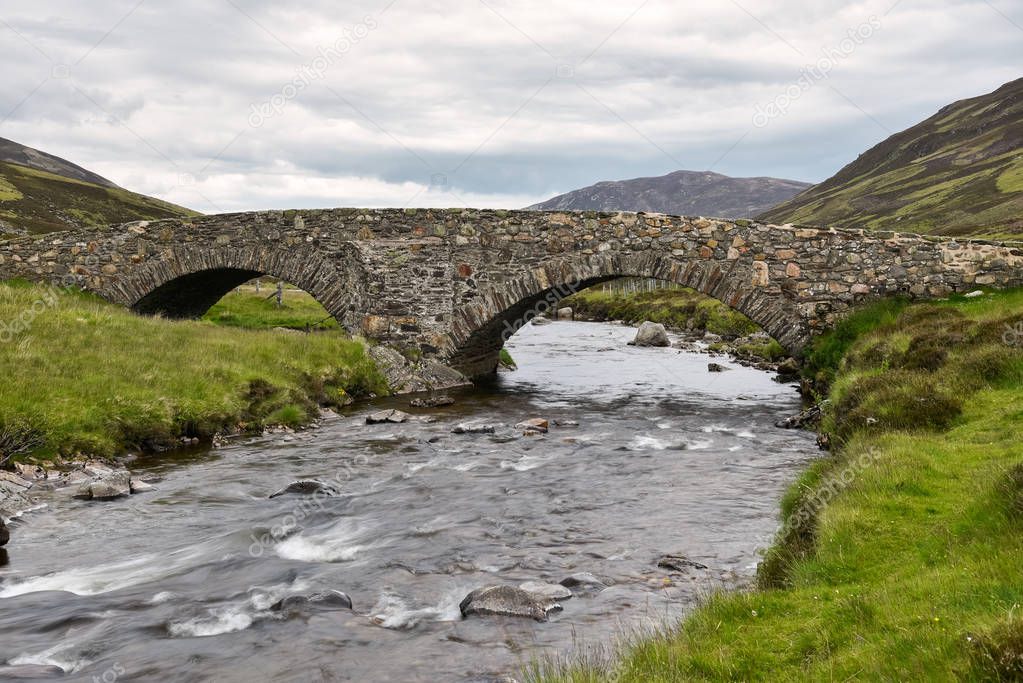 Historic stone bridge over a small river in the Scottish Highlands on a cloudy summer day. Aberdeenshire, Scotland, UK.