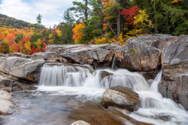 Majestic waterfall along a mountain riverwith stunning autumn colours in background on a cloudy autumn morning. White mountains, NH, United States. clipart