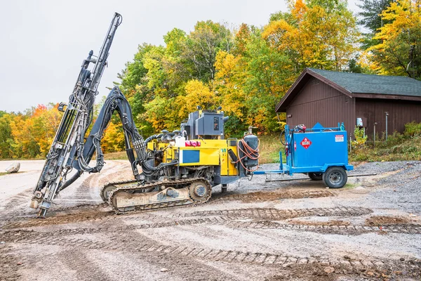 Heavy earth drilling machine in a construction site with colourful trees in background on an overcast autumn day