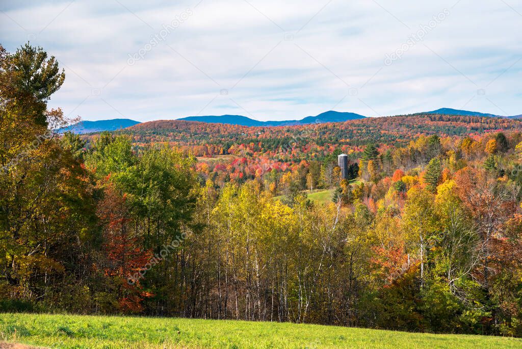 Beautiful rolling hills covered in deciduous forests at the peak of fall foliage dotted with grassy fields on a sunny autumn day. Groton State Forest, VT, USA.