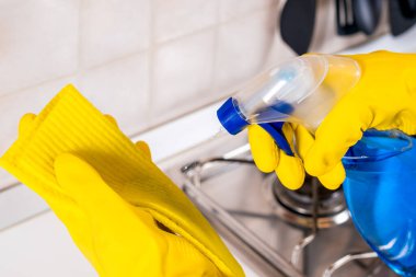 Sarı lastik eldiven giyen bir kadının mutfak atölyesini temizleme süngeri ve sprey dezenfektanla temizlerken çekilmiş bir fotoğrafı. Covid-19 yayılan önleme ve hijyen kavramı.