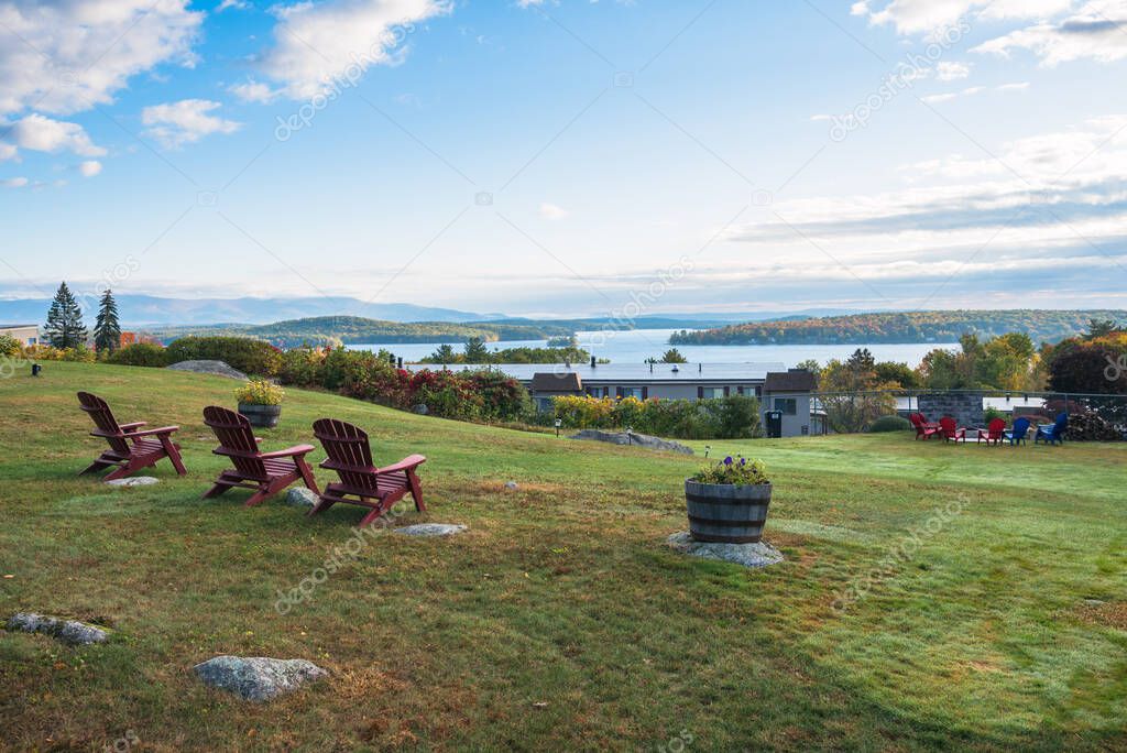 Empty adirondack chairs in a row in a lawn overlooking a majestic mountain lake on a clear autumn morning