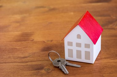 Bir ev modelinin ve anahtarların kırsal ahşap bir masanın üzerinde durduğunu gördüm. Gayrimenkul satın alma kavramı.