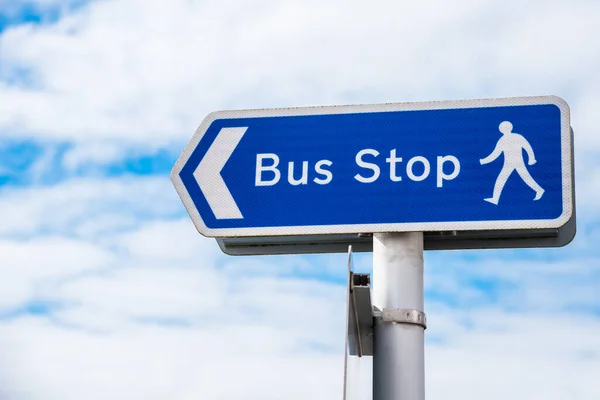 Weathered directional sign pointing the way to a bus stop with cloudy sky in background. Orkney Islands, Scotland, UK.