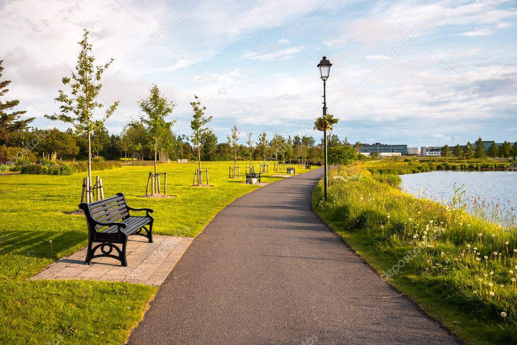 Deserted path lined with metal benches along a pond in a public park at sunset. Reykjavik, Iceland.