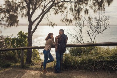 Orta yaşlı bir çift okyanus manzaralı bir parkta kalır ve konuşur..