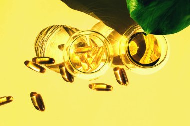 Omega-3 kapsüllü balık yağı ve sarı arka planda canavar yaprağı olan cam bardaklarda yağ. Sağlık ve güzellik kavramı