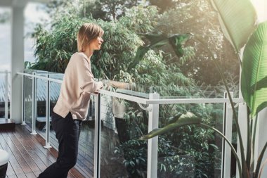 Orta yaşlı bir kadın balkondan tropikal manzaranın tadını çıkarıyor.