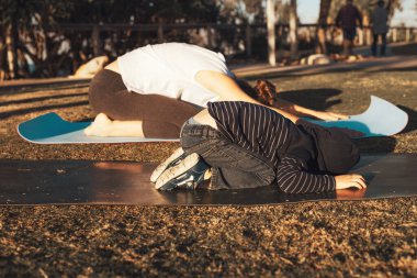 Genç anne ve oğlu gün batımında şehir parkında jimnastik yapıyor ve esneme hareketleri yapıyor.