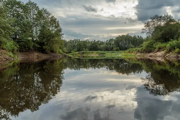 Řeka se zelenými břehy pod zamračený oblohou — Stock fotografie