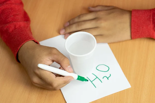Adolescente escribe fórmulas químicas marcador en una hoja blanca con un vaso de agua —  Fotos de Stock