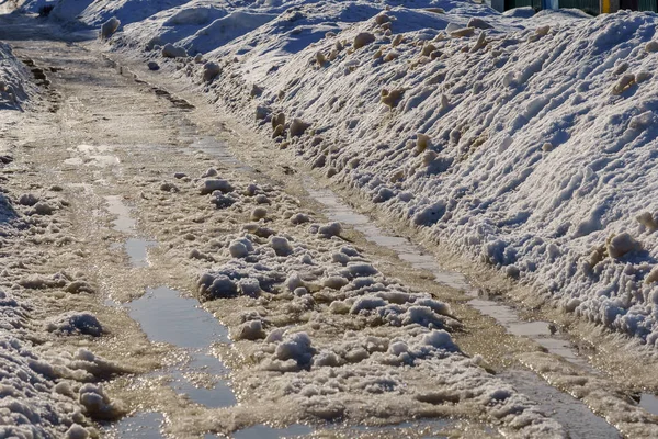 Zimowa droga pokryta śniegiem i lodem z kałużami i rutami — Zdjęcie stockowe