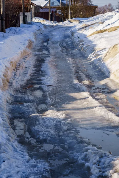 Schnee- und eisbedeckte Winterstraße mit Pfützen und Spurrillen — Stockfoto