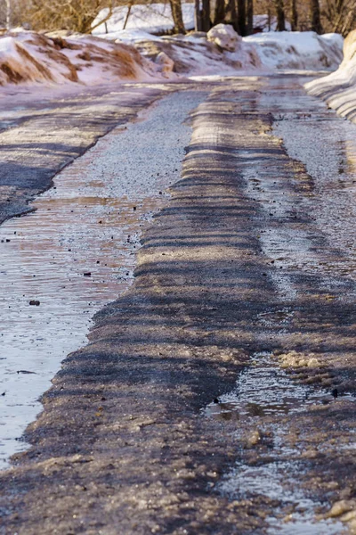 Schnee- und eisbedeckte Winterstraße mit Pfützen und Spurrillen — Stockfoto