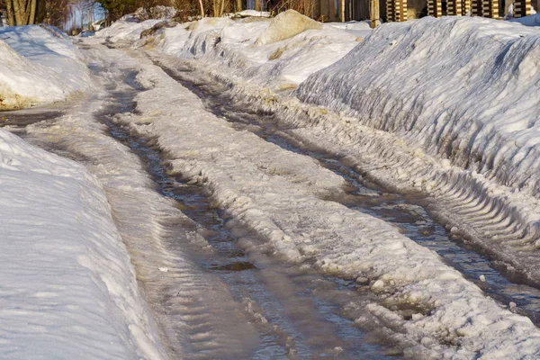 Zimowa droga pokryta śniegiem i lodem z kałużami i rutami — Zdjęcie stockowe
