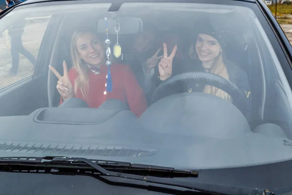 Молодые женщины на переднем сиденье автомобиля улыбаются и машут через лобовое стекло — стоковое фото