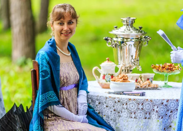 Animator i en gammal klänning hälsar gästerna i parken vid bordet med en samovar Stockfoto