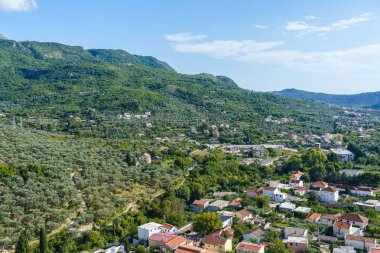 Dağların arkasında, kiremitlerle döşenmiş tavanlar ve yeşillikler...