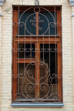 Eski bir dövme demir ızgara, dekoratif güvenlik öğesi. Güzel tuğla duvar resimleri ile eski bir ev pencere eski bir ızgara. Klasik metal kafes sahte. Ahşap eski pencere.