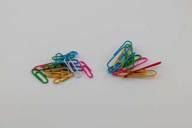 Two distinct piles of vibrant paper clips are placed on a plain white surface, showcasing various colors and sizes, ideal for office or school organization.