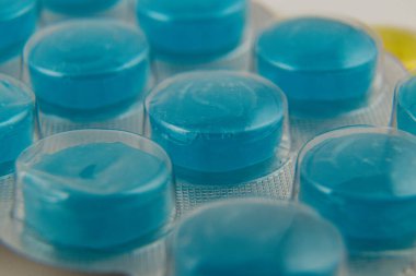 Mavi yuvarlak tabletler açık renkli bir yüzey üzerinde açık plastik bir kabarcık paketi içinde düzenlenir. Paketleme tabletlerin canlı rengini ve şekillerini vurgular.