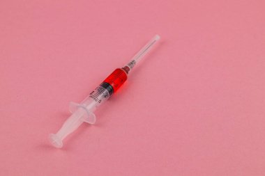 A syringe filled with bright red liquid rests on a smooth pink surface, showcasing its sleek design and vibrant colors, emphasizing themes of health and science.