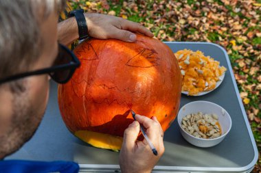 A person is focused on carving a pumpkin, adding a spooky design while surrounded by autumn leaves, showcasing creativity and seasonal spirit.
