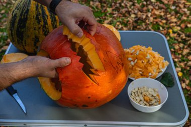 Hands skillfully carve a pumpkin in a backyard while surrounded by fallen leaves, showcasing autumn's creativity and festive spirit during a bright afternoon.