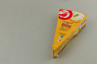 Lviv Ukraine 05.22.25 A wedge of brie cheese is presented on a smooth gray surface. The cheese packaging is yellow and features details about the product, including expiration date.