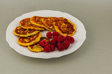 Fluffy pancakes are arranged neatly on a white plate, accompanied by vibrant fresh raspberries, creating an appealing breakfast scene.