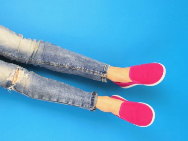 Mavi zemin üzerinde yırtık kot pantolon kırık bir diz ile kızın bacakları. Üstten görünüm. Modern spor stil kavramı.