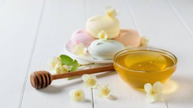 Renkli macaroons ve bal bir beyaz tahta masaya Yasemin çiçek ile. Tatlı köyü masada bileşimi.