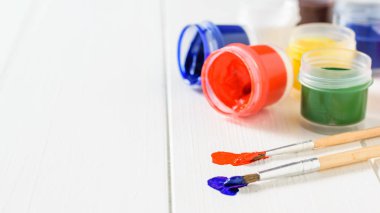 İki fırçalar mavi ve kırmızı boya ve guaj Beyaz ahşap bir masa üzerinde bir kavanoz. Yaratıcı kiti. Hobi ve stil.