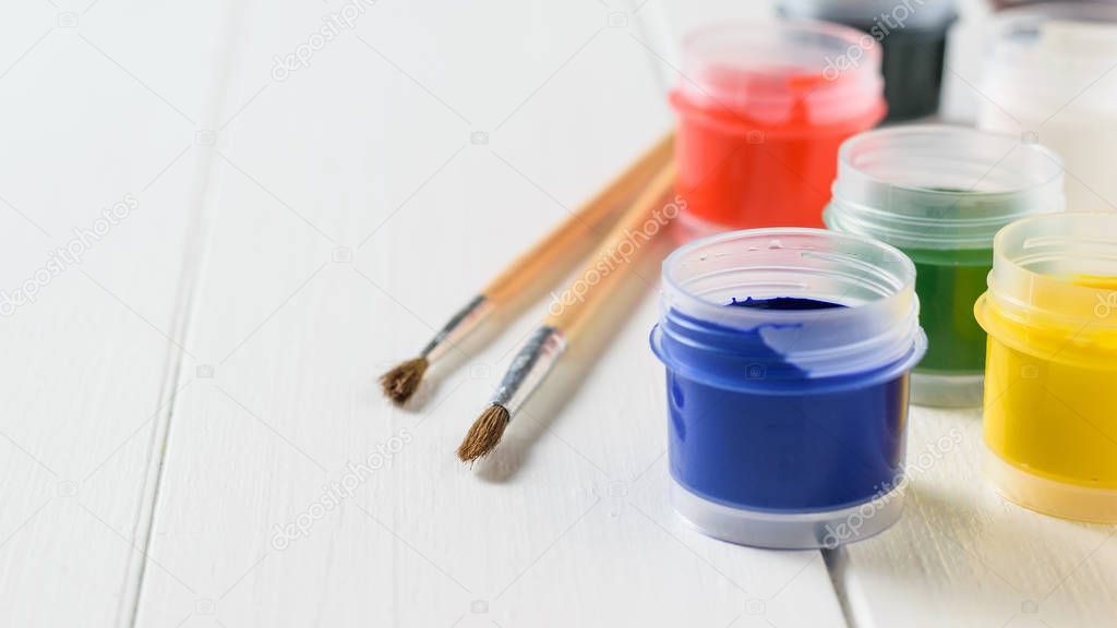 Open jars of gouache and brushes on a white wooden table.. Creative kit. Hobby and style.