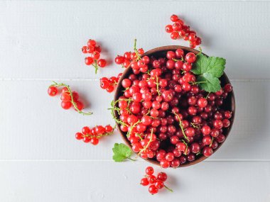Dağınık kırmızı kuş üzümü çilek ve bir kase çilek Beyaz ahşap bir masa üzerinde. Sağlıklı doğal gıda kavramı. Düz yatıyordu.
