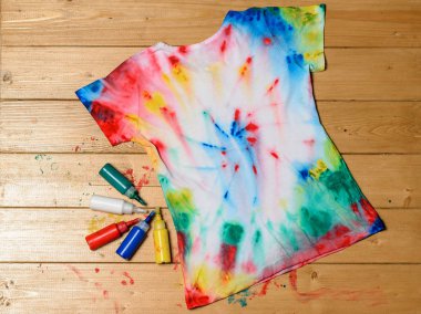 T-shirt painted in tie dye style on a wooden table. White clothes painted by hand. clipart