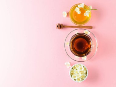 Bitkisel çay, bal, Yasemin çiçekleri ve bir tahta kaşık pembe bir tablo. Sabah kahvaltı bileşimi. Bahar çay kompozisyon beyaz bir tablo. Düz yatıyordu. Üstten görünüm.