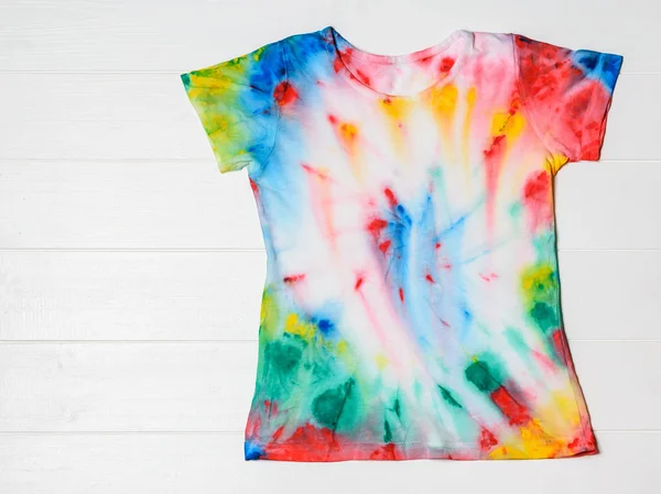 T-shirt painted in tie dye style on a wooden table. White clothes painted by hand. Flat lay. The view from the top. Place for text.