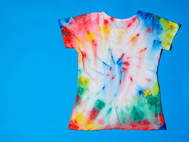 Mavi bir arka plan üzerinde kravat boya tarzında T-shirt boyalı. Beyaz giysiler elle boyanmış. Üstten görünüm. Düz yatıyordu.
