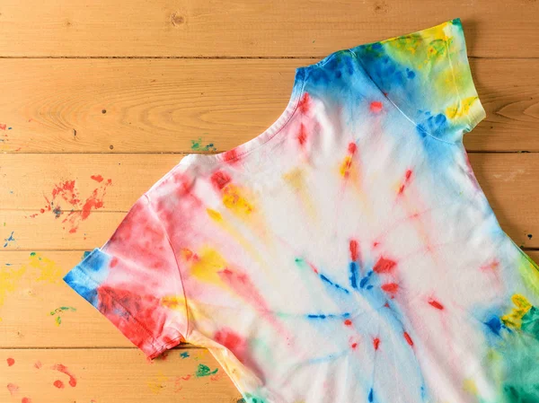 T-shirt tarzı ahşap bir masaüstü üzerine kravat boya boyalı. Beyaz giysiler elle boyanmış. Düz yatıyordu. Üstten görünüm.