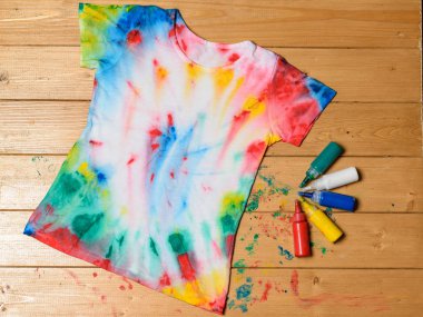 T-shirt painted in tie dye style on a wooden table. White clothes painted by hand. clipart
