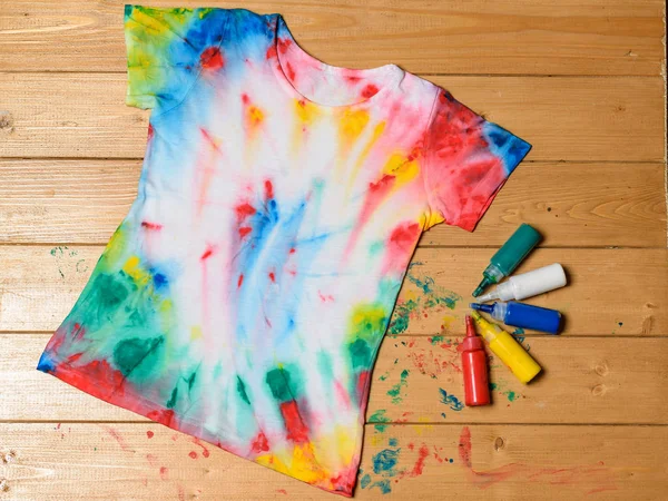 T-shirt painted in tie dye style on a wooden table. White clothes painted by hand.