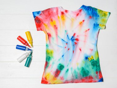 Tüpleri giysileri ve t-shirt için boya bir beyaz tahta masada kravat boya tarzında. Beyaz giysiler elle boyanmış. Düz yatıyordu.