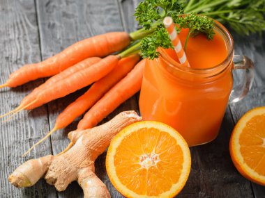 Bir bardak taze havuç kokteyl bardağı taşıran damla, maydanoz, zencefil kökü ve koyu ahşap bir masa üzerinde portakal ile güler yüzlü. Sağlıklı beslenme kavramı.