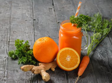 Bir bardak taze havuç kokteyl bardağı taşıran damla, maydanoz, zencefil kökü ve koyu ahşap bir masa üzerinde portakal ile güler yüzlü. Sağlıklı beslenme kavramı.