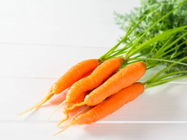 Bunch of fresh carrots on a white wooden table. The concept of vegetarian food with natural raw products.