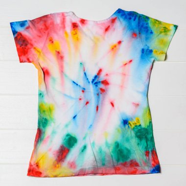 T-shirt painted in tie dye style on a white wooden table. White clothes painted by hand. clipart