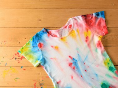 T-shirt in tie dye style on a wooden table stained with paint. White clothes painted by hand. Flat lay. The view from the top. clipart